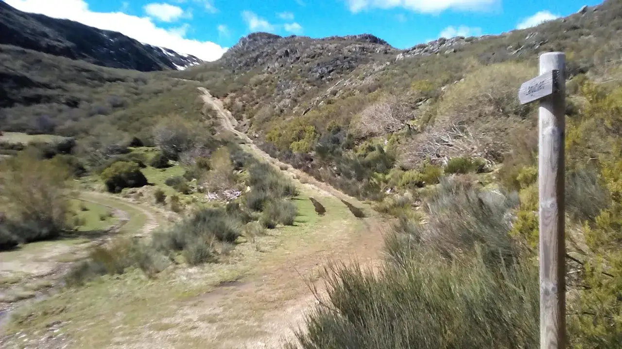 Ruta de senderismo en un paisaje montañoso, con un poste de madera que indica