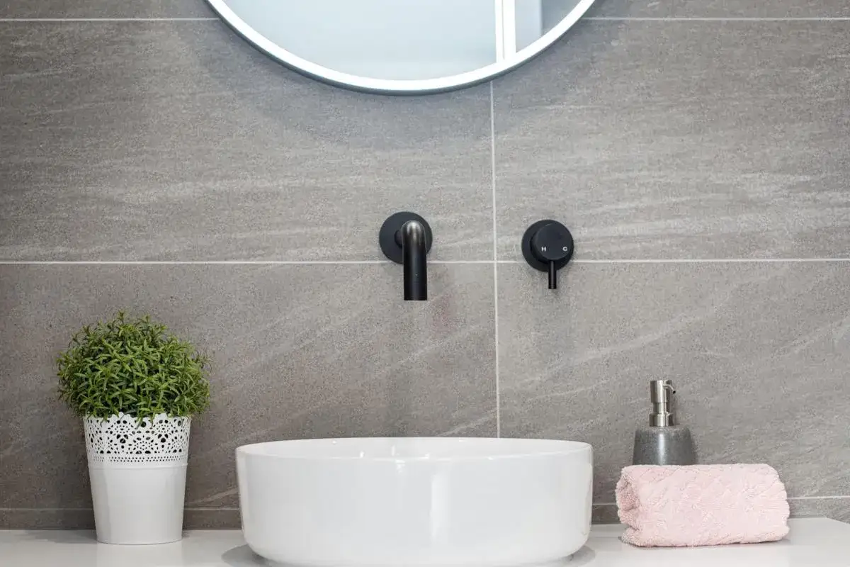 Rubinetto lavabo a parete: pro e contro di un design moderno. Un lavabo bianco, un rubinetto nero e un tocco di verde.