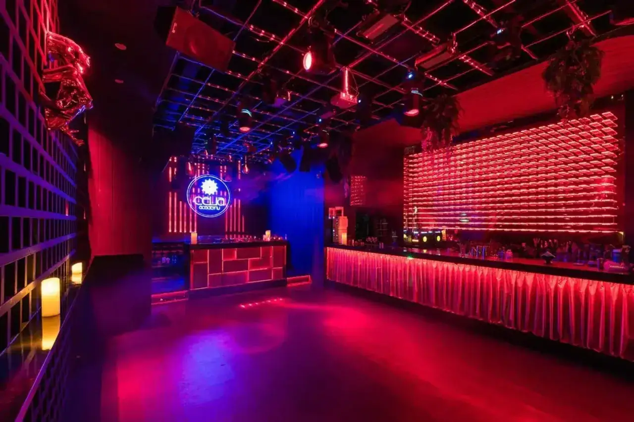 Interno di un locale notturno con luci rosse e blu, bancone bar illuminato e logo al neon. Perfetto per idee di nomi per locali notturni.