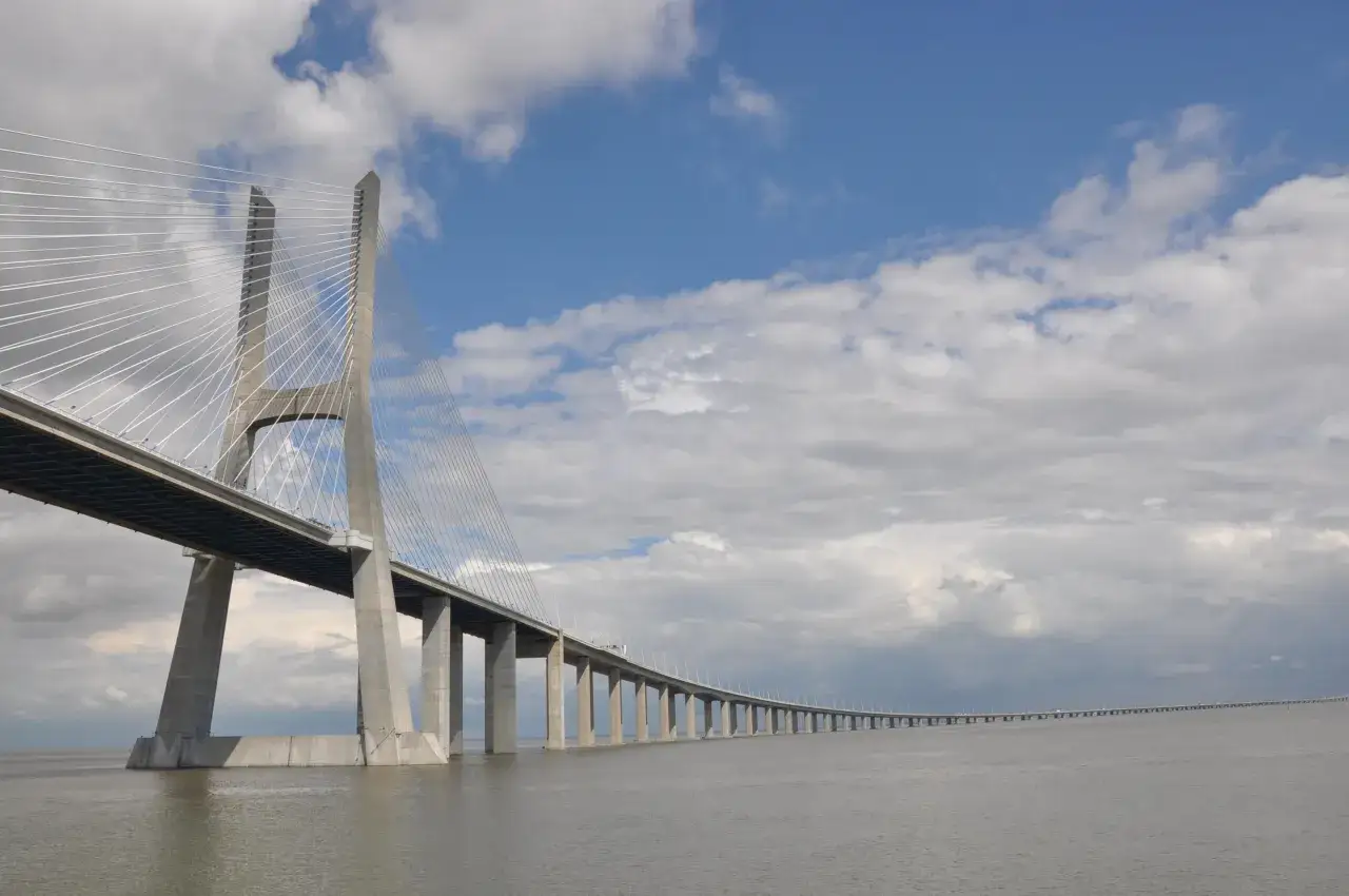 El **puente Vasco da Gama** se extiende majestuoso sobre el río Tajo, con sus pilares de hormigón y cables de acero desafiando el cielo nublado.