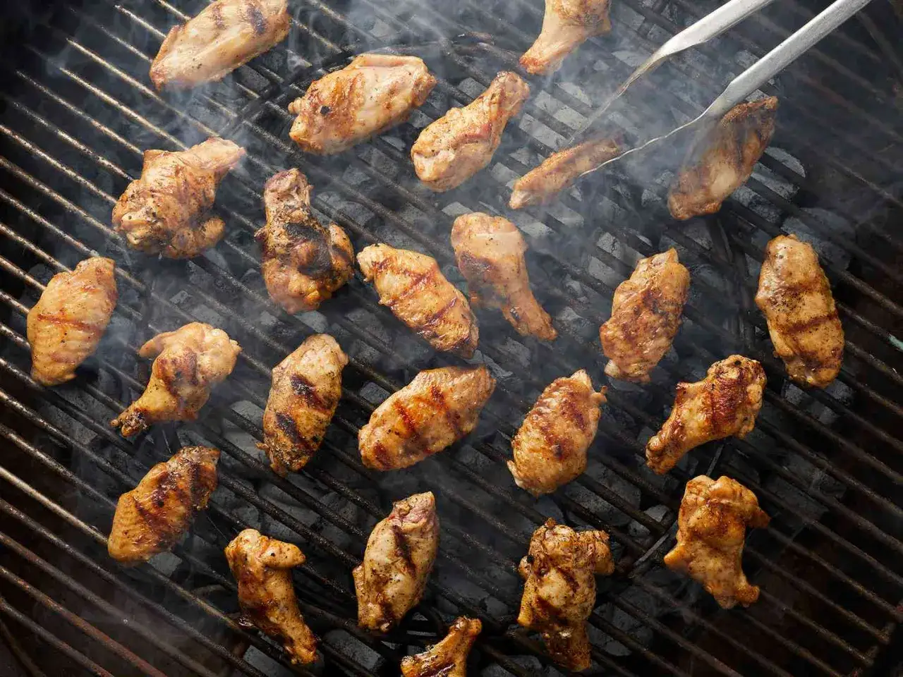 Ailes de poulet grillées sur un barbecue, fumantes et dorées. Le temps de cuisson parfait pour des ailes de poulet savoureuses.
