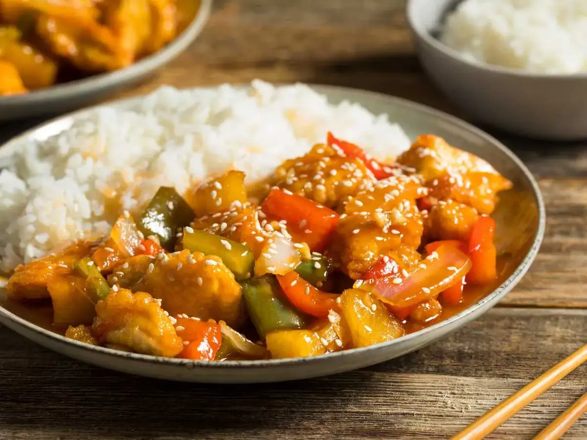 Delicioso pollo agridulce con arroz blanco, pimientos y piña, espolvoreado con semillas de sésamo.