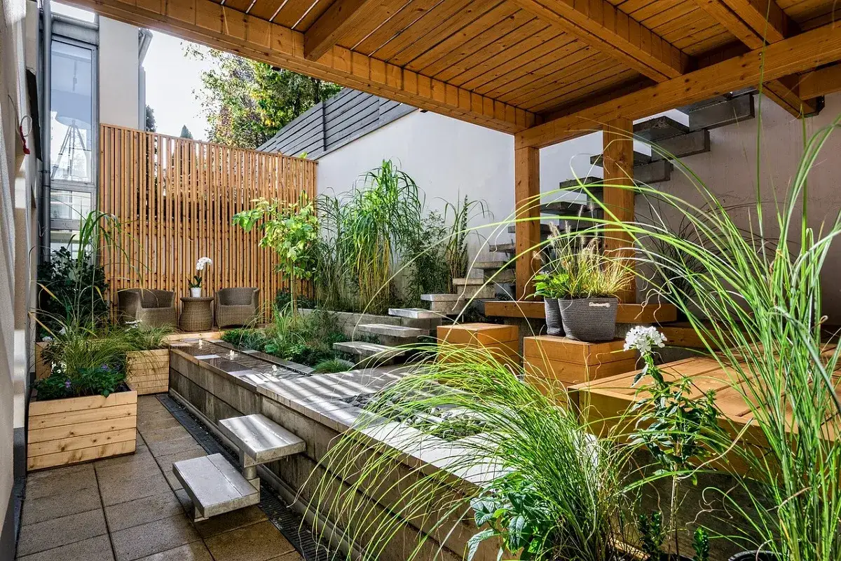 Giardini fioriti idee: un angolo zen con vasca d'acqua, gradini in pietra, piante rigogliose e arredi in legno sotto una tettoia.