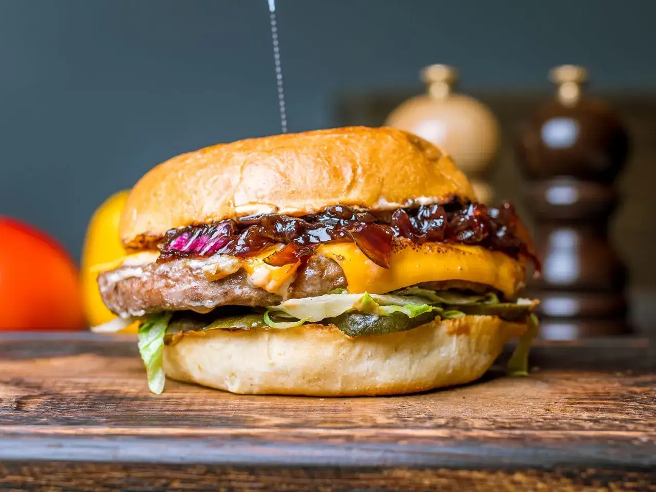 Un succulent steak burger avec fromage fondu, oignons caram&eacute;lis&eacute;s et cornichons, sur une planche en bois.