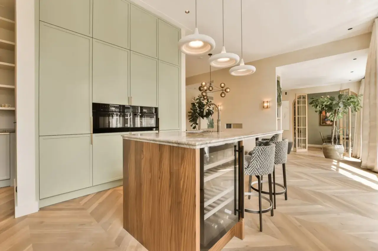Cuisine moderne avec &icirc;lot central, armoires vert p&acirc;le et un magnifique parquet au sol en chevrons.