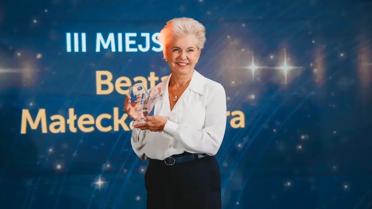 Beata Małecka-Libera z dumą prezentuje statuetkę III miejsca na tle błękitnego ekranu z gwiazdami.