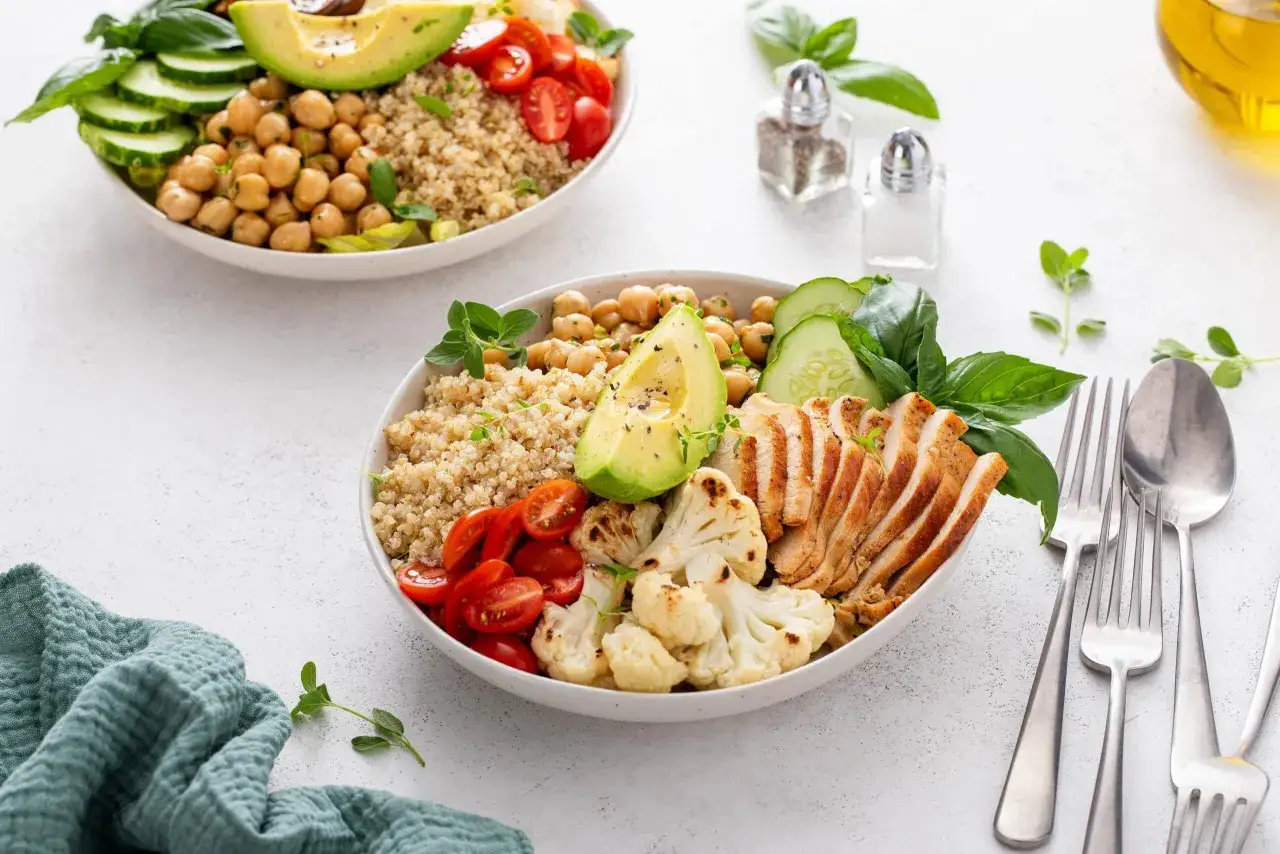Due ciotole di quinoa con pollo, ceci, avocado, pomodorini, cavolfiore e cetrioli. Chi soffre di diverticolite può mangiare il riso, ma la quinoa è un'ottima alternativa.