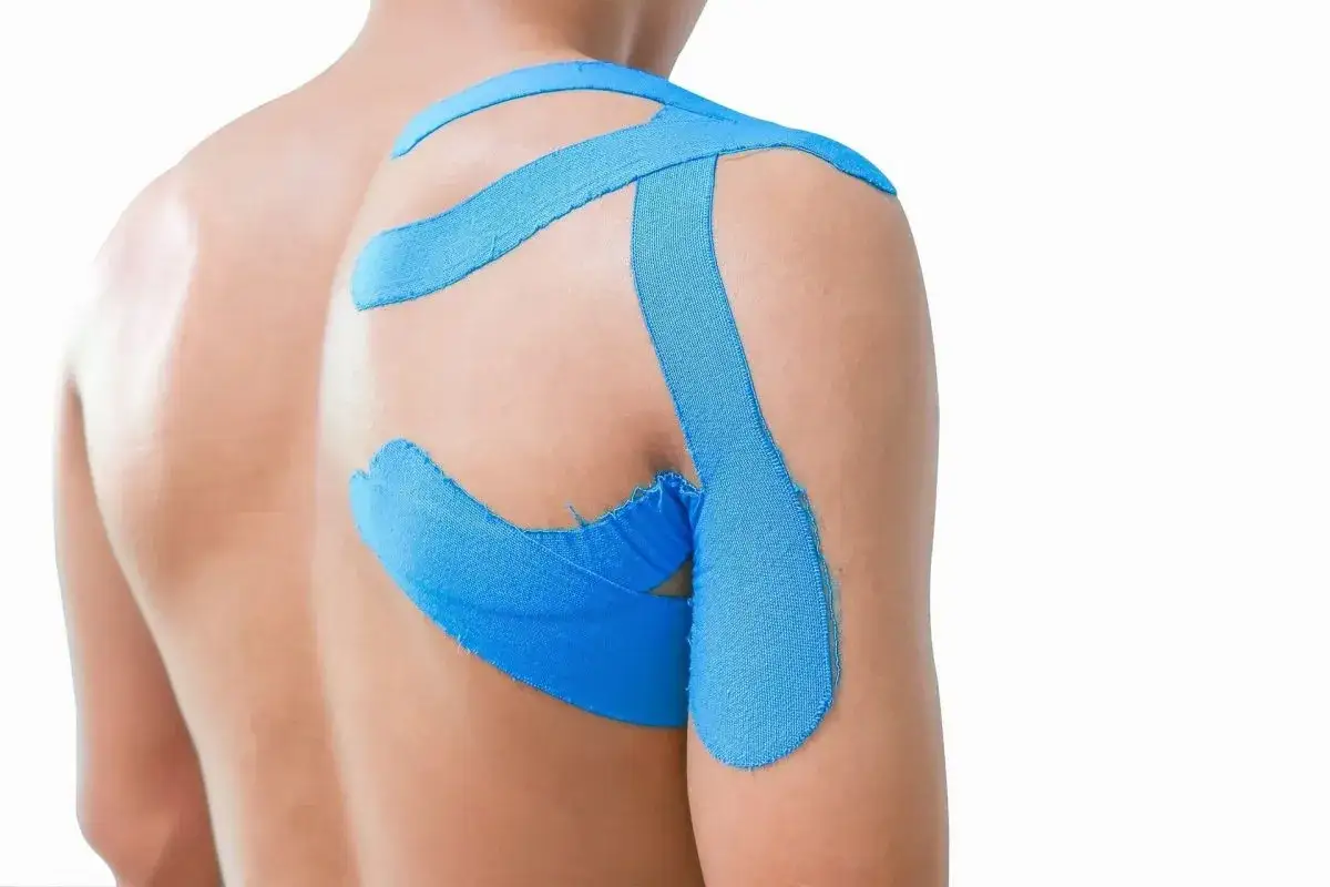 Spalla di un uomo con taping blu applicato per supporto. Il taping si pu&ograve; mettere da soli per alleviare il dolore.