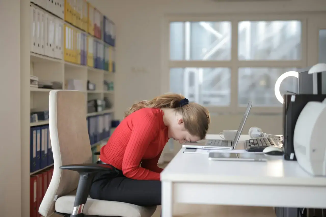 Frau mit roten Pullover legt Kopf auf Laptop. Sie fragt sich, was tun gegen Antriebslosigkeit im B&uuml;ro.