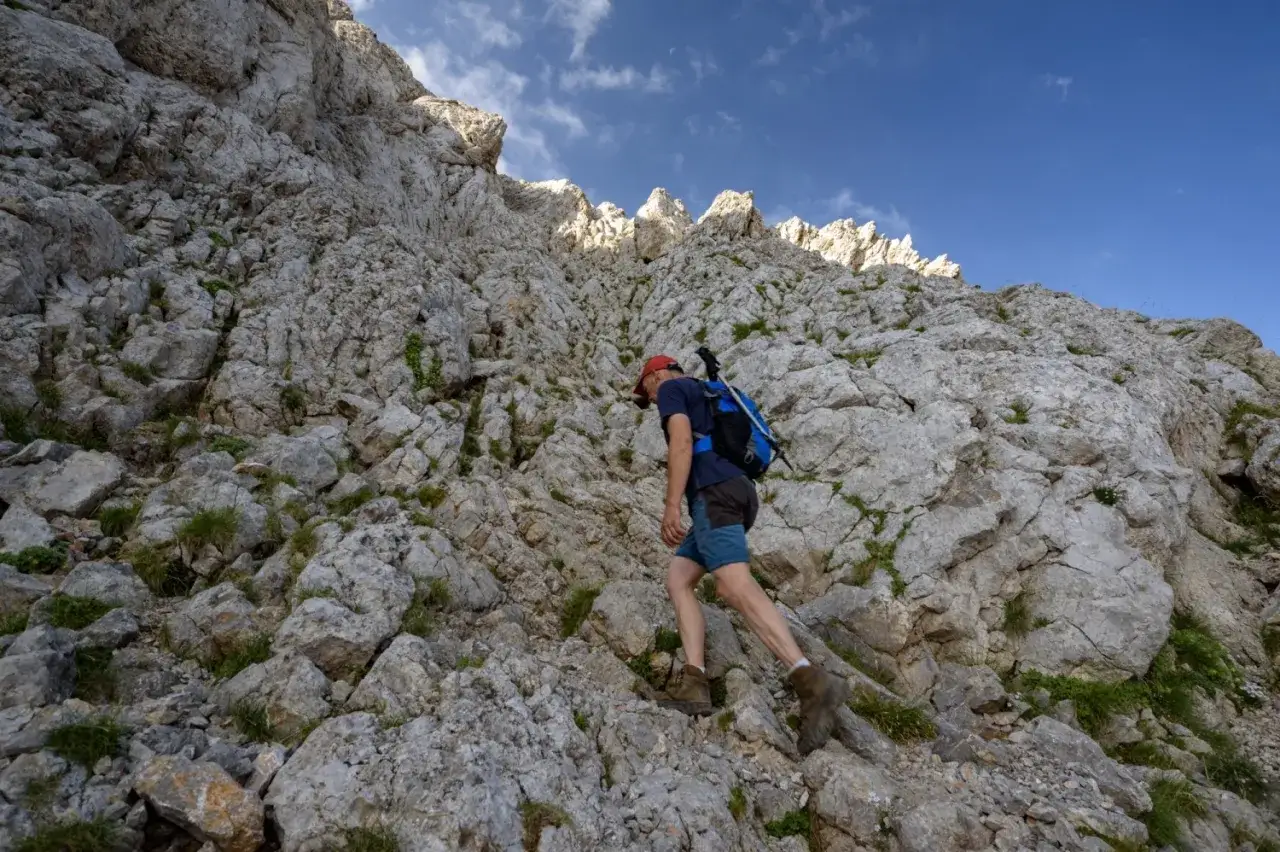 Un excursionista asciende por una ladera rocosa y empinada, con el Pedraforca imponente al fondo.