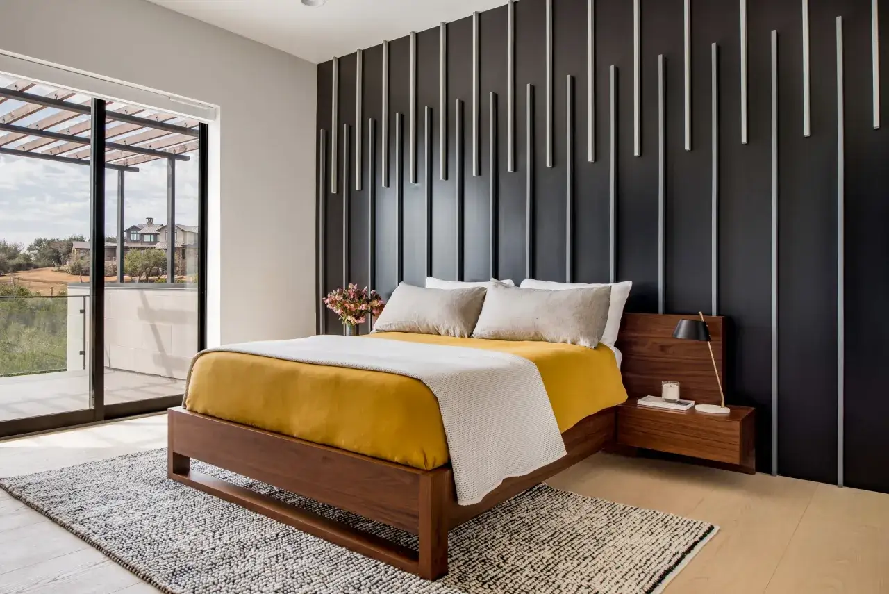 Dormitorio moderno con cama de madera, ropa de cama amarilla y manta blanca. La pared negra tiene un diseño vertical que recuerda a pinturas de pared abstractas.