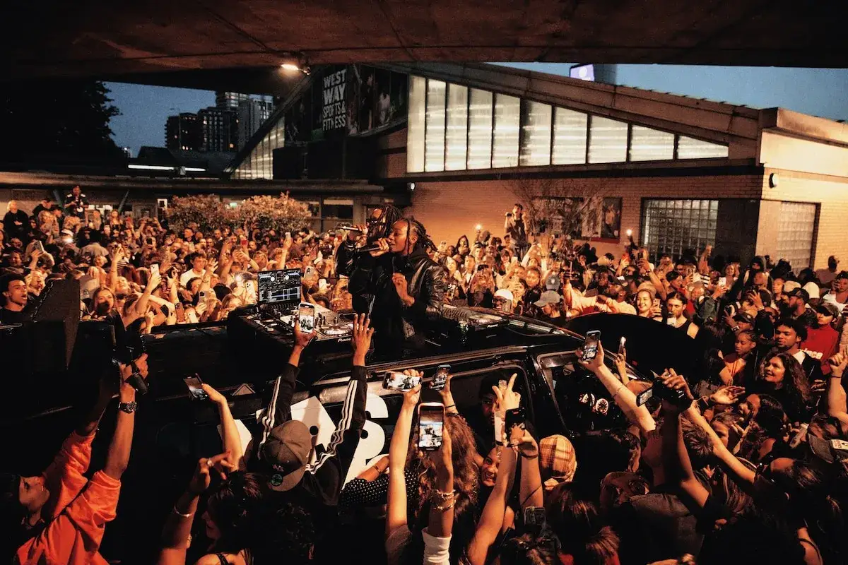 Un concerto all'aperto a Londra, con un DJ e un cantante su un'auto, circondati da una folla entusiasta che filma con i cellulari. L'atmosfera ricorda le migliori discoteche londinesi.
