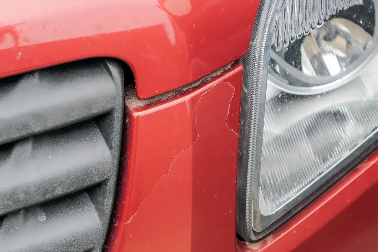 Pęknięty lakier na czerwonym zderzaku obok reflektora. Zastanawiasz się, ile kosztuje lakierowanie zderzaka po takiej szkodzie?
