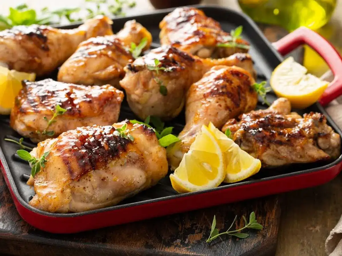Jugosos contramuslos de pollo a la parrilla, dorados y con hierbas frescas, acompa&ntilde;ados de gajos de lim&oacute;n.