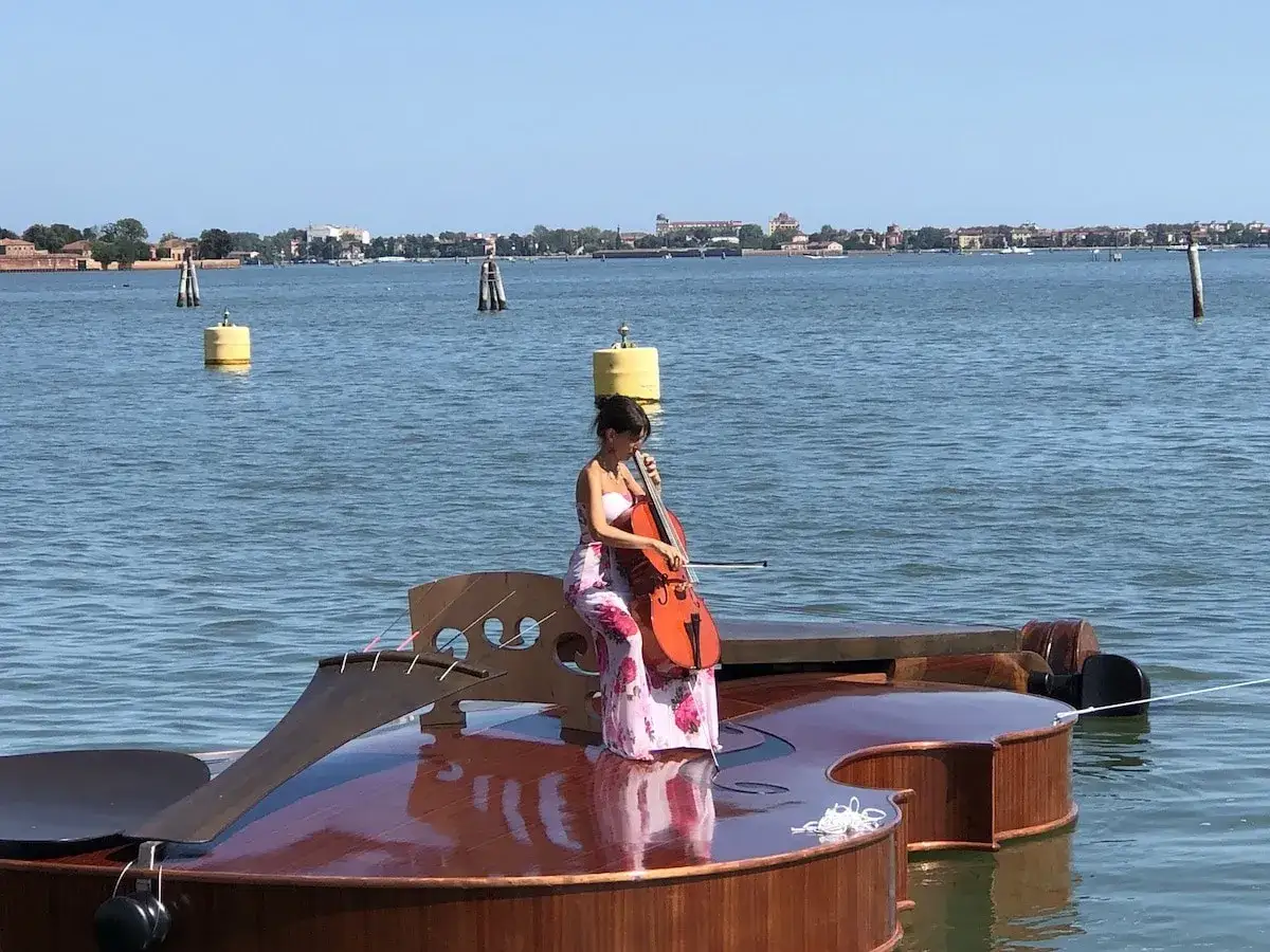 Une violoncelliste joue sur une immense structure en forme de violoncelle flottant sur l'eau, une &oelig;uvre de Livio de Marchi.