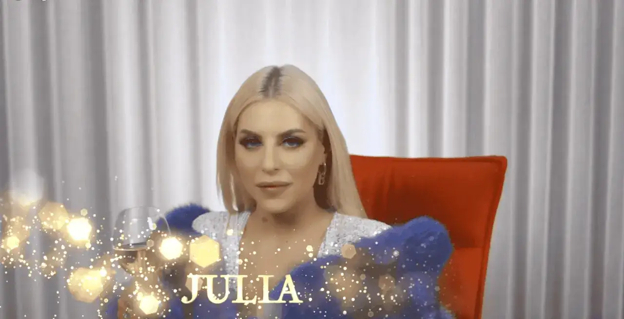 Julia von Stein w błyszczącej kreacji, z kieliszkiem wina, otoczona złotymi iskierkami.