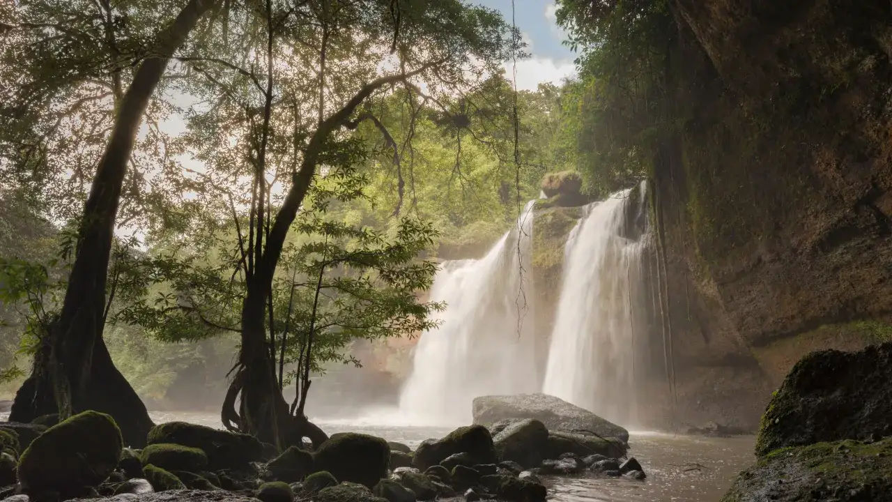 Ein rauschender Wasserfall im Dschungel von Khao Yai, umgeben von &uuml;ppiger Vegetation und moosbewachsenen Felsen.