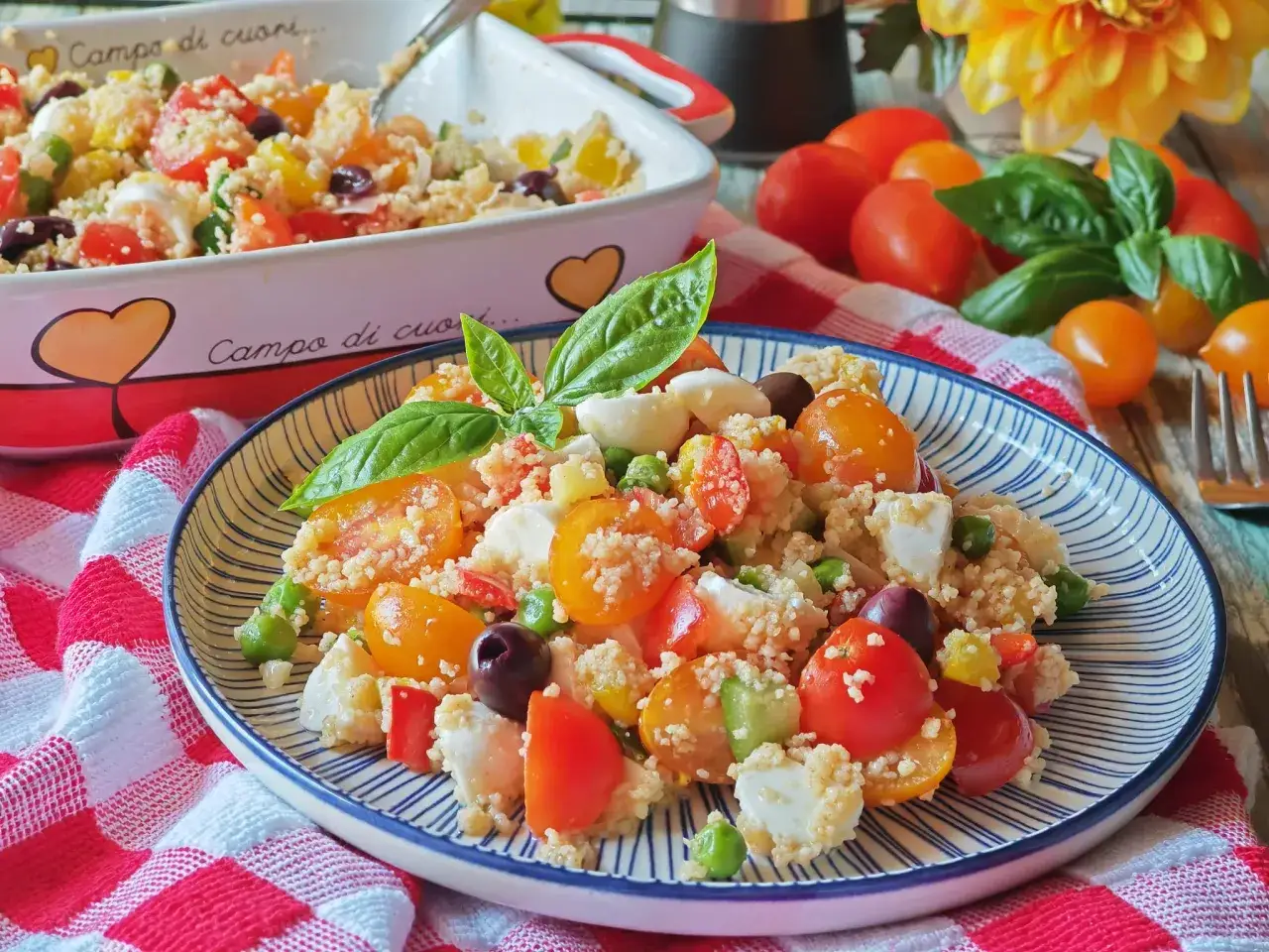 Un piatto colorato di cous cous freddo con pomodorini, mozzarella, olive e basilico, perfetto per un pasto estivo.