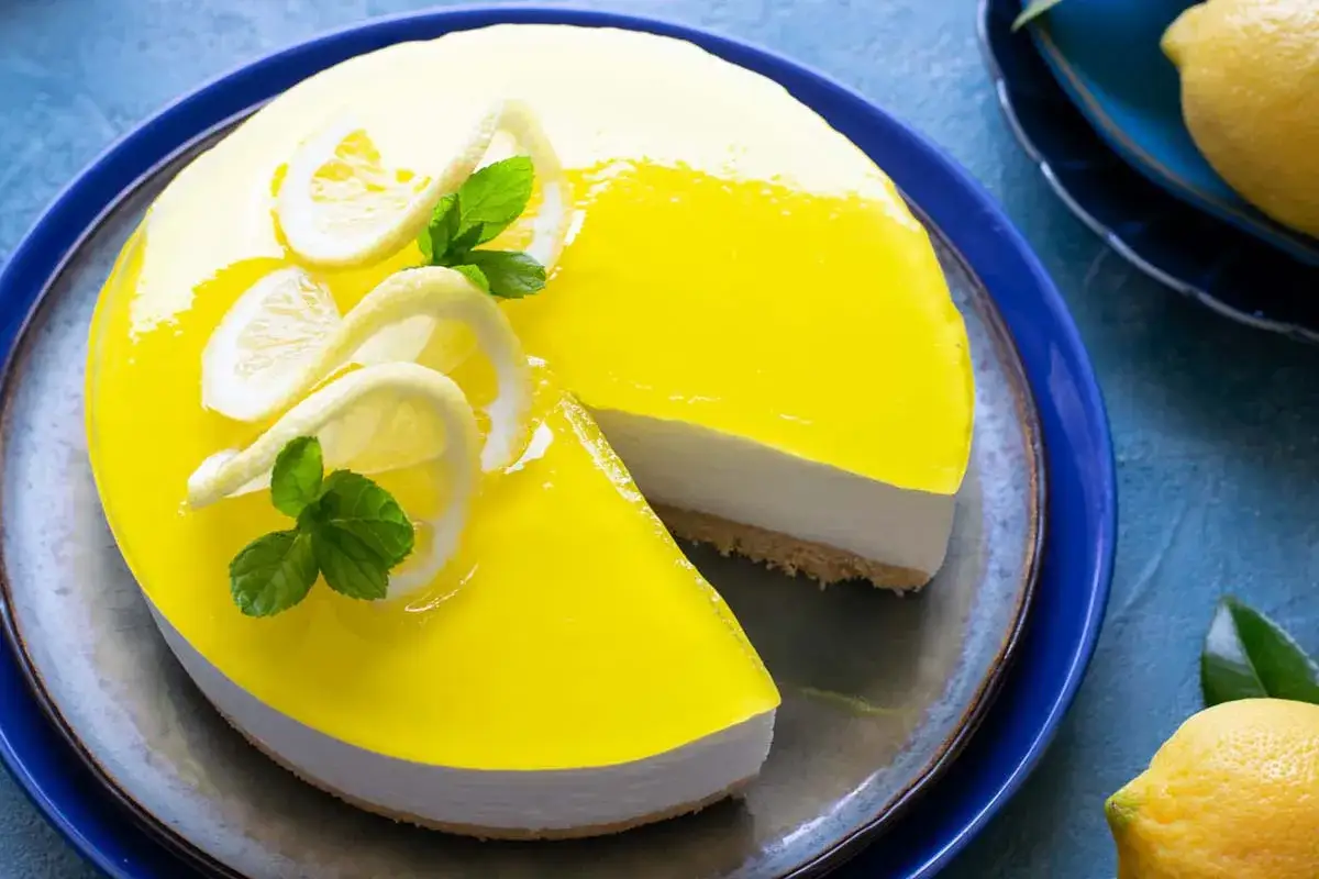 Una fetta di torta fredda al limone, con glassa gialla brillante, decorata con fettine di limone e menta.