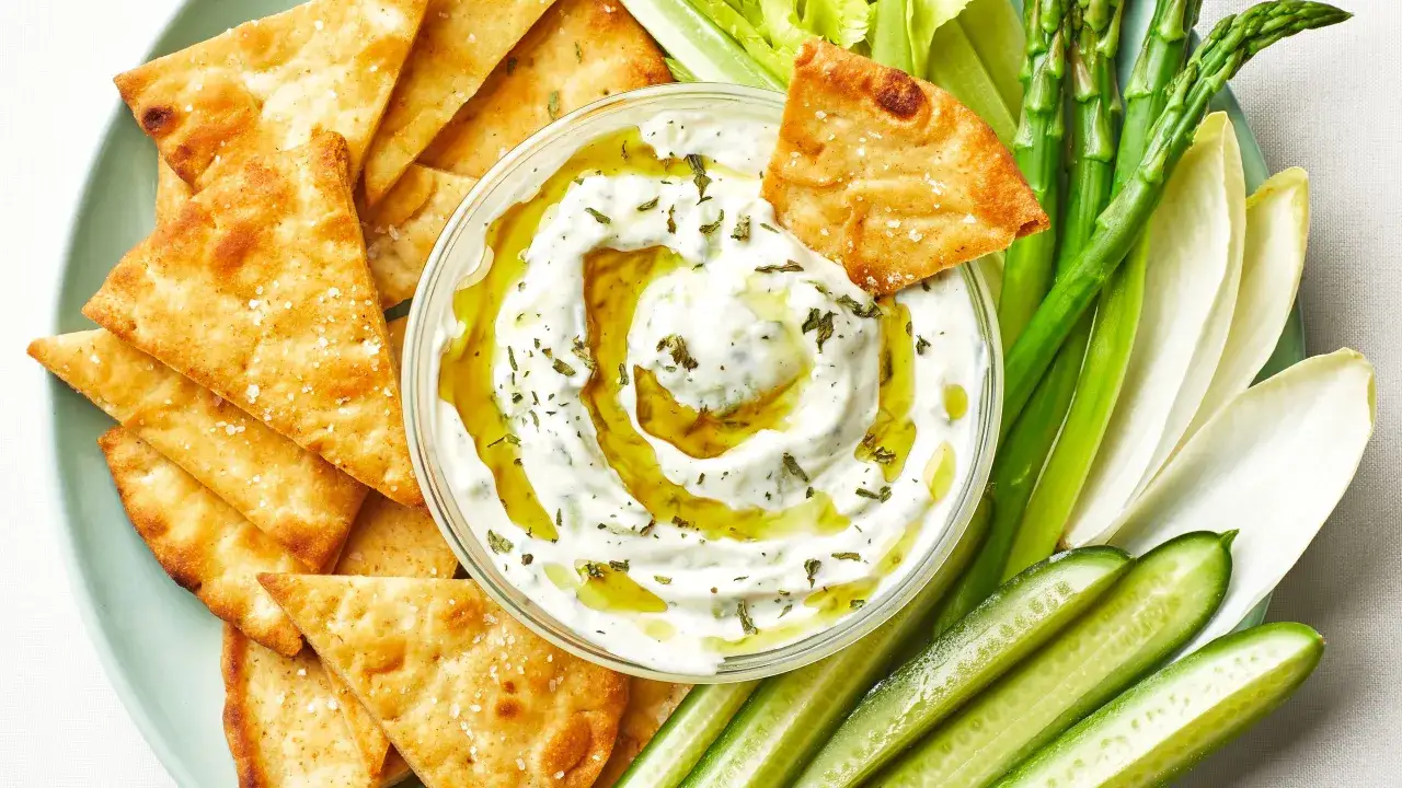 Chrupiące chipsy pita i świeże warzywa, takie jak ogórek, szparagi i cykoria, zanurzone w kremowym sosie tzatziki z oliwą.