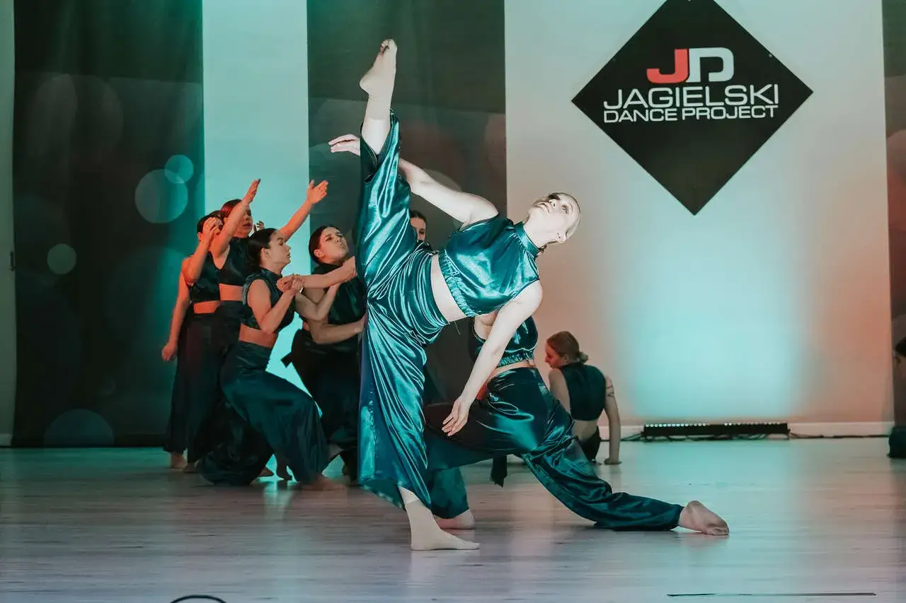 Tymek Sobczyk w akcji z tancerzami Jagielski Dance Project. Grupa wykonuje dynamiczny układ w błyszczących, turkusowych strojach.