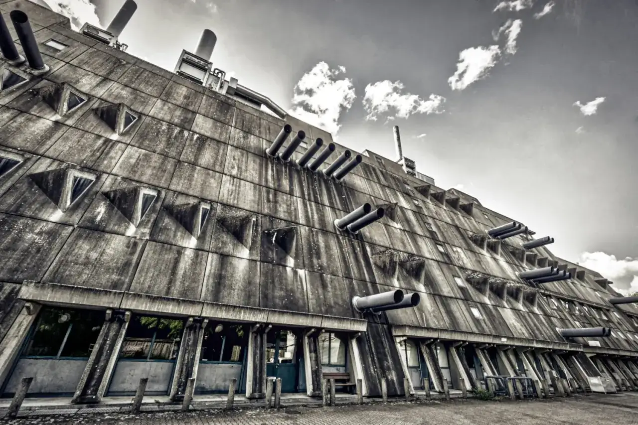 Betonriese im **Brutalismus Berlin**: Ein Geb&auml;ude mit dreieckigen Fenstern und Rohren, das an eine futuristische Festung erinnert.