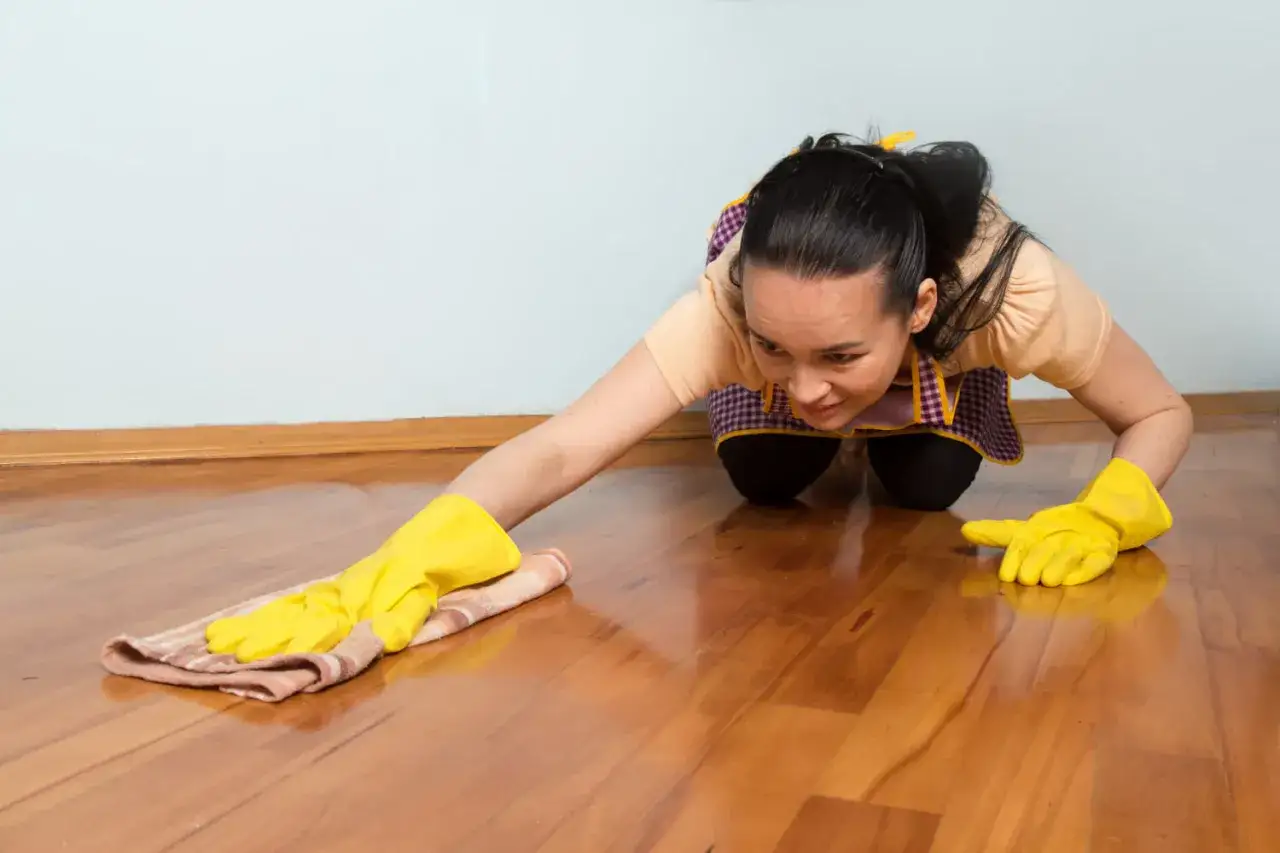 Mujer con guantes amarillos limpiando suelo laminado con un pa&ntilde;o.