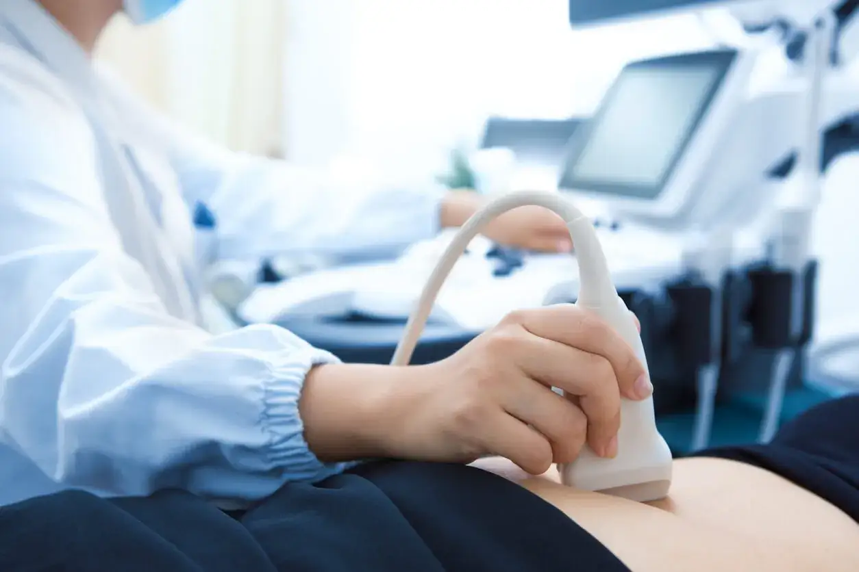 Lekarz wykonuje badanie USG, przykładając głowicę aparatu do brzucha pacjenta. Obraz pokazuje nowoczesny sprzęt do diagnostyki ultradźwiękami.