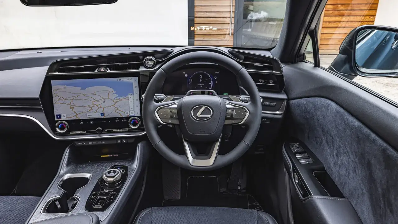 Wnętrze Lexus RZ z dużym ekranem nawigacji i cyfrowymi zegarami. Kierownica z logo Lexus i przyciskami sterowania.