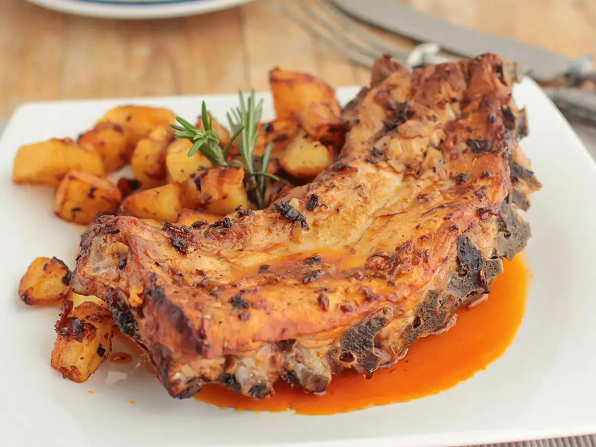 Costillas de cerdo jugosas y doradas, acompa&ntilde;adas de patatas asadas y una ramita de romero. &iexcl;Un plato delicioso!