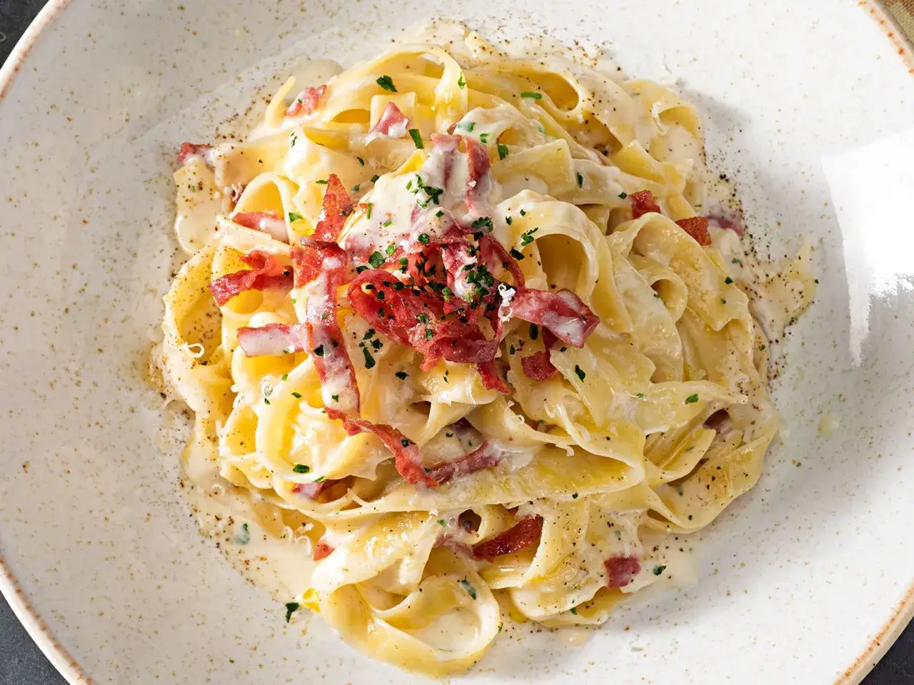 Fettuccine cremose con pancetta croccante e un tocco di Philadelphia, guarnite con prezzemolo fresco e pepe nero.