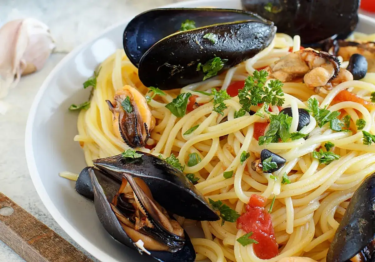 Deliciosa pasta con mejillones y tomate, adornada con perejil fresco. Un plato que huele a mar y a Italia.