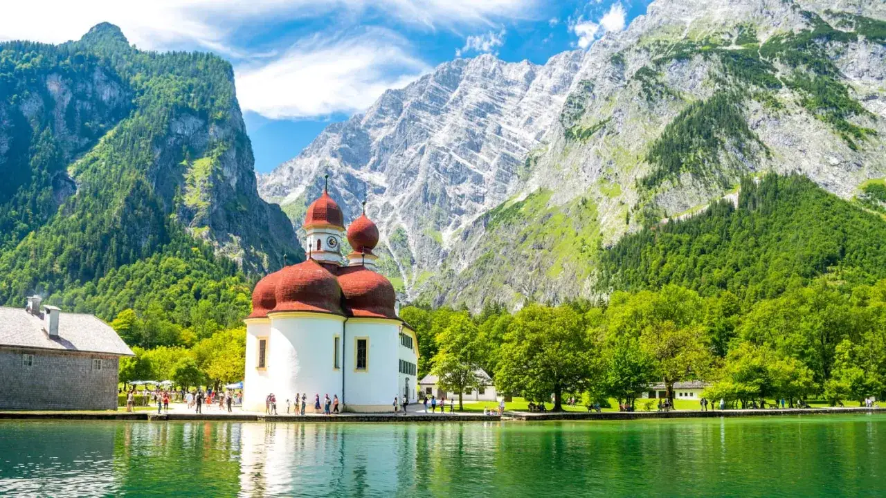 Idyllischer Sommerurlaub in Bayern: Wallfahrtskirche St. Bartholomä am Königssee vor imposanter Bergkulisse.
