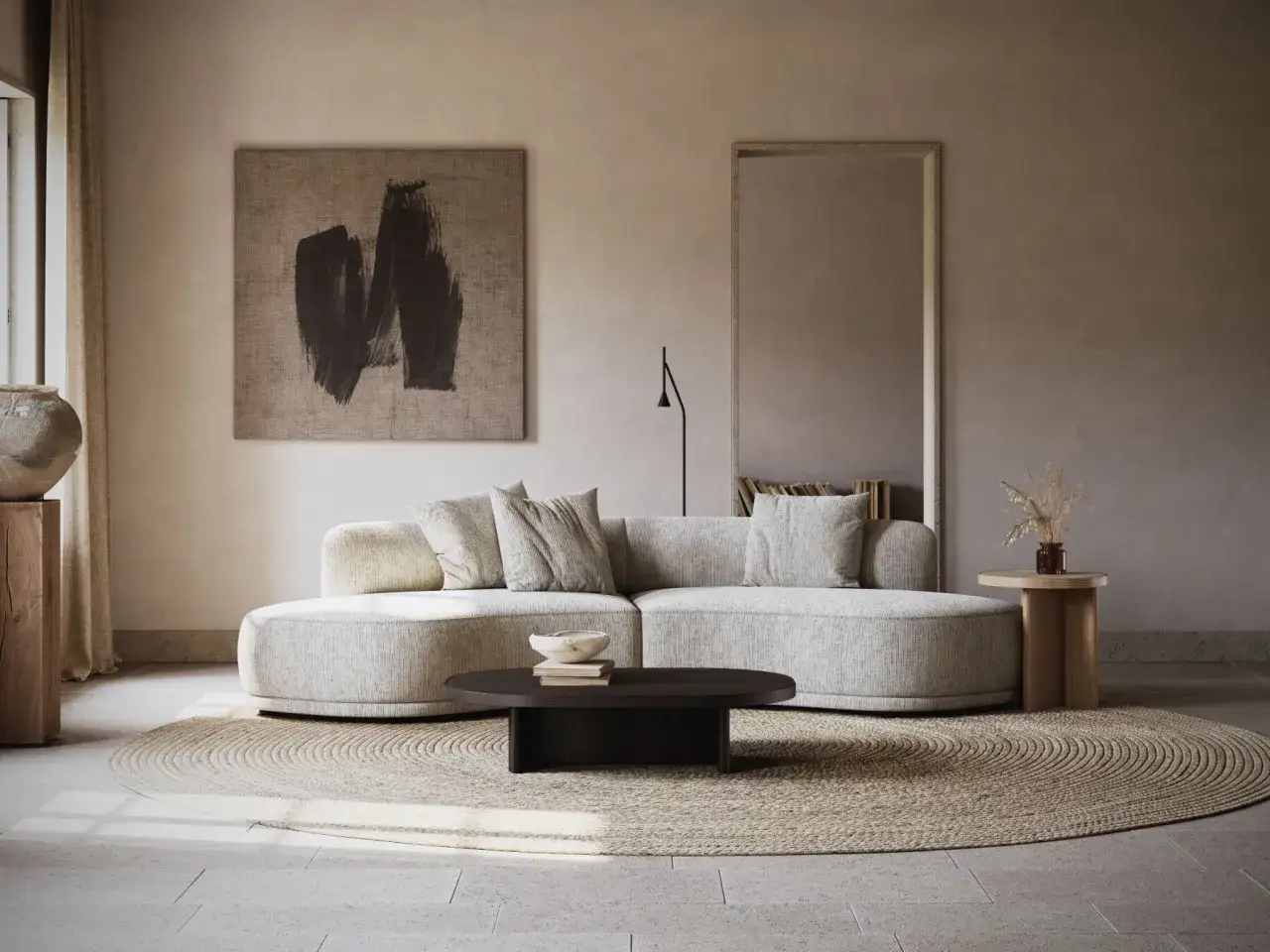 Salon cosy aux couleurs neutres chaudes. Canapé arrondi, tapis rond en jonc de mer, table basse sombre et art abstrait.
