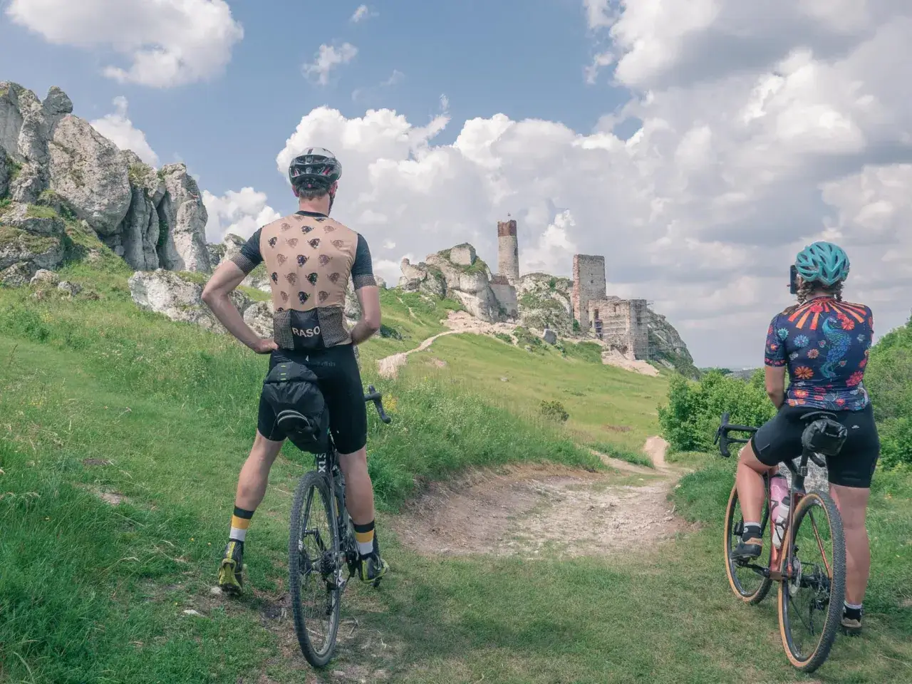 Dwie osoby na rowerach podziwiają ruiny zamku na wzgórzu. Idealne miejsce na odkrywanie tras rowerowych Częstochowa.