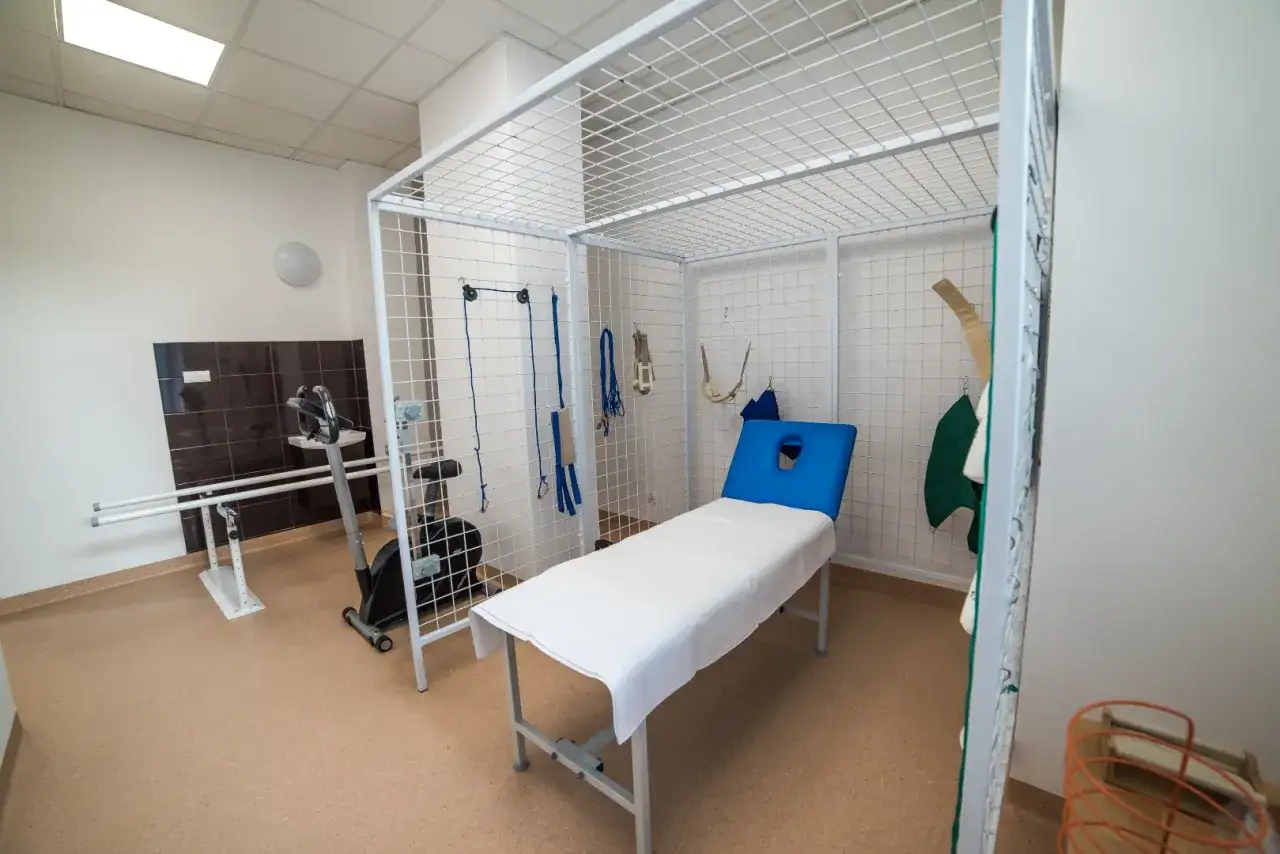 Gabinet kinezyterapii co to? Pok&oacute;j rehabilitacyjny z leżanką, rowerkiem stacjonarnym, poręczami i przyrządami do ćwiczeń.