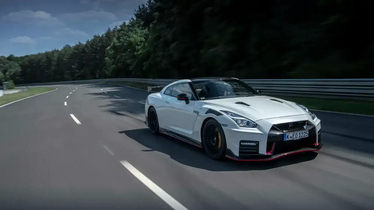 Biały Nissan GT-R Nismo pędzi po torze wyścigowym, otoczony zielenią lasu.