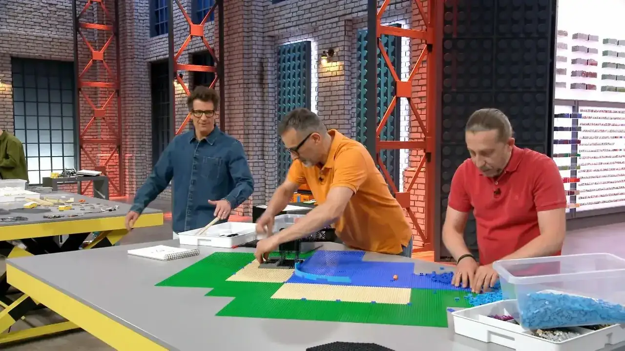 Drei M&auml;nner bauen mit bunten Lego-Steinen. Einer sortiert blaue Steine, ein anderer legt gr&uuml;ne und beige Platten aus. Ein dritter schaut zu. Hier sind die Lego Masters!
