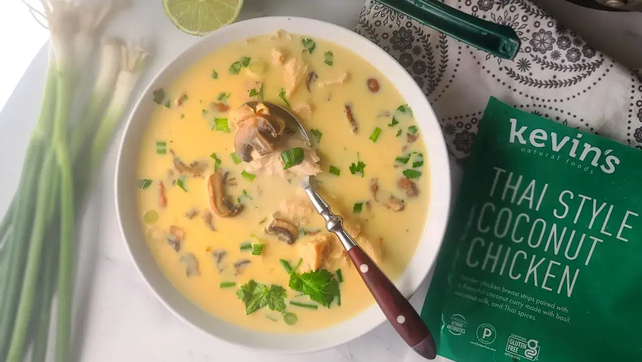 Aksamitna zupa tom kha z kurczakiem i grzybami, ozdobiona szczypiorkiem i kolendrą. Obok opakowanie 