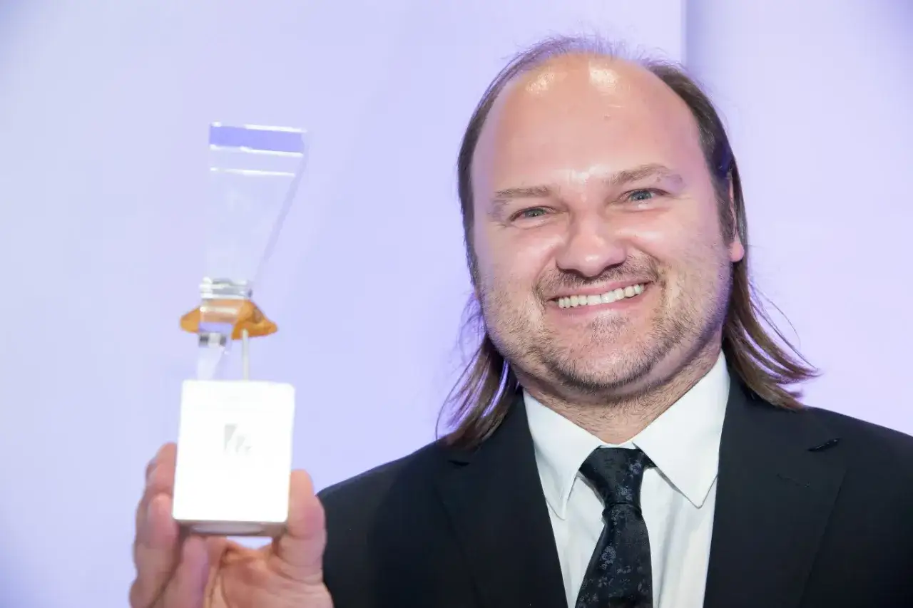 Uśmiechnięty mężczyzna w garniturze trzyma statuetkę. Czy to nagroda za rolę, która pomoże odpowiedzieć na pytanie, ile zarabia aktor?