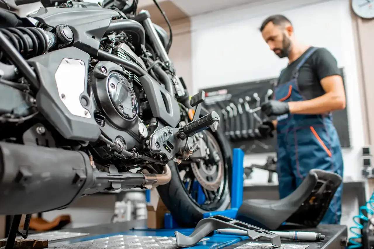 Meccanico in officina, con tuta blu, si prepara a pulire il motore di una moto. Attrezzi a vista.
