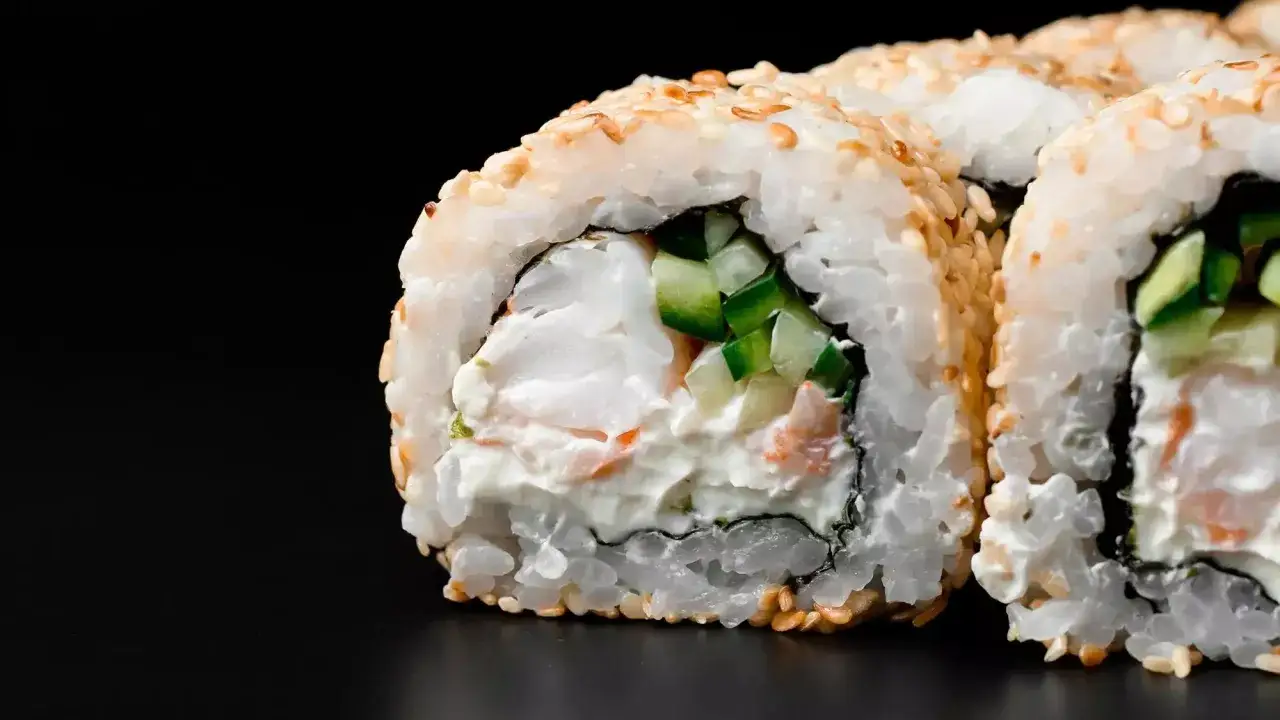 Rolka california sushi z krewetkami, awokado i ogórkiem, obsypana sezamem.