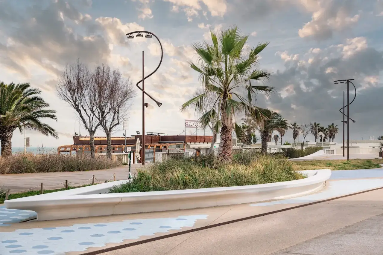 Un viale moderno nel parco del mare Rimini, con palme, alberi spogli e un cielo nuvoloso.