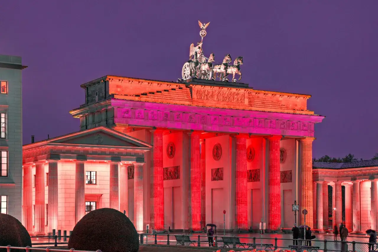Das Brandenburger Tor in Berlin, die Stadt der Lichter, erstrahlt in rotem und pinkem Licht unter einem violetten Himmel.