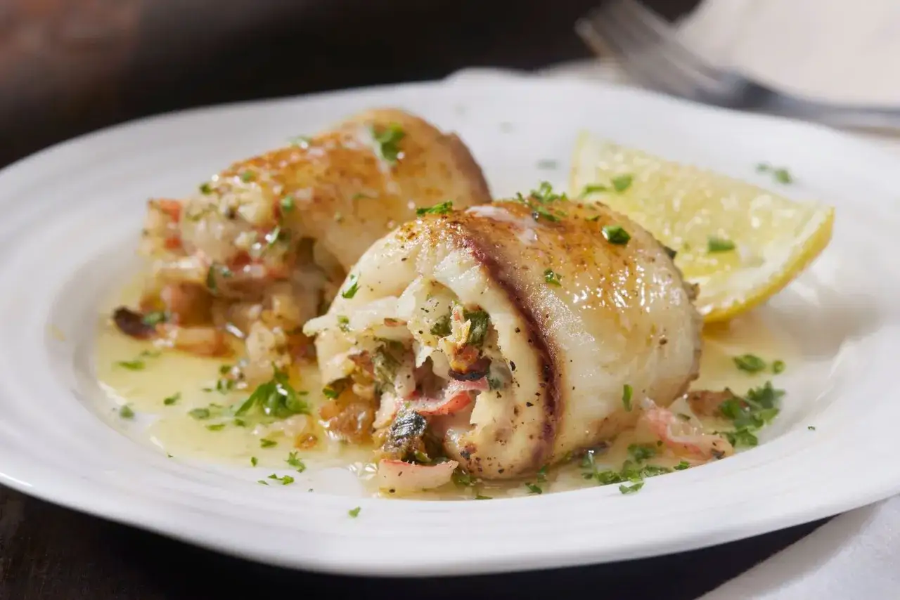 Deliziosi involtini alla messinese ripieni di pesce e verdure, serviti su un piatto bianco con spicchio di limone e prezzemolo tritato.
