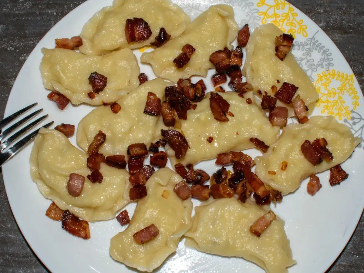 Pyszne pierogi galicyjskie z chrupiącym boczkiem na białym talerzu. Obok widelca.
