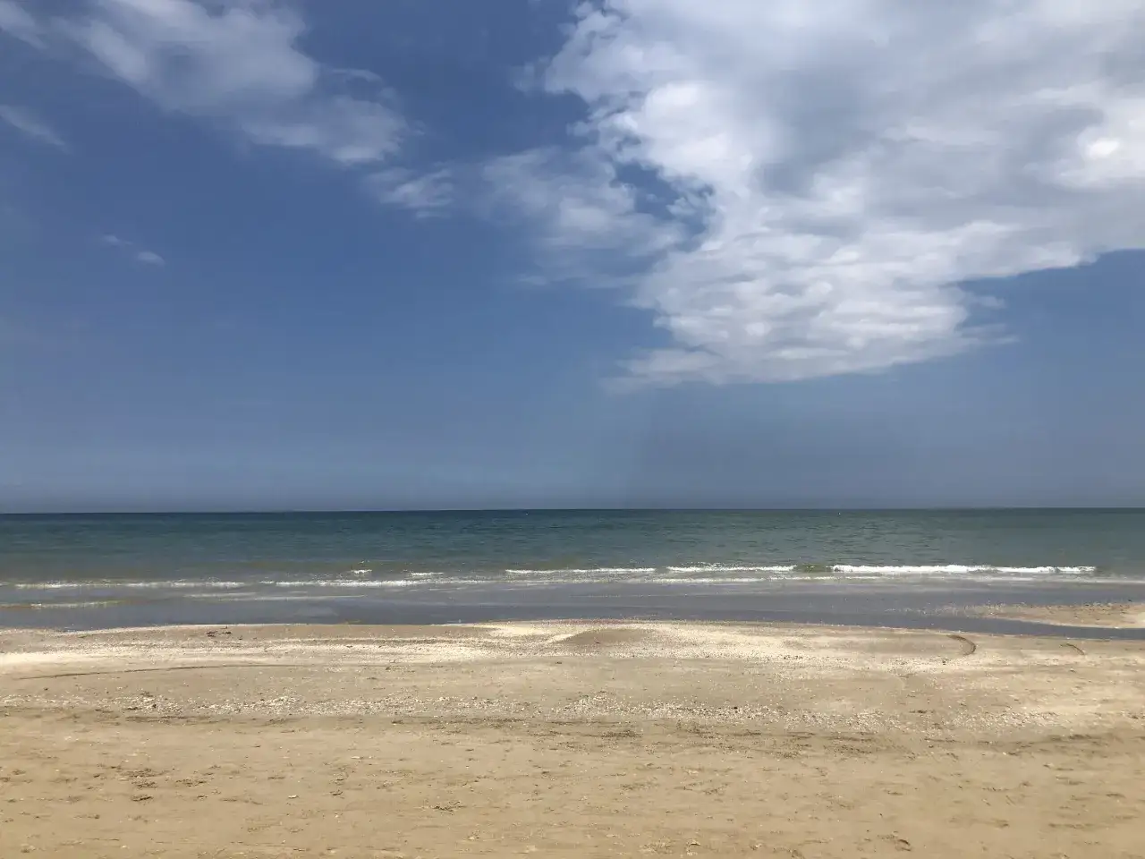 Spiaggia dorata e mare calmo a Rimini a settembre, con nuvole bianche che danzano nel cielo azzurro.