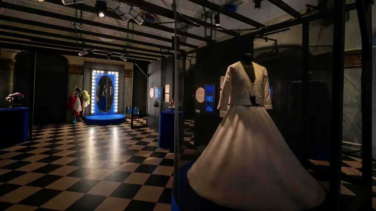 En vit dansklänning visas upp i en monter på Dansmuseet Stockholm. Golvet har ett schackrutigt mönster.