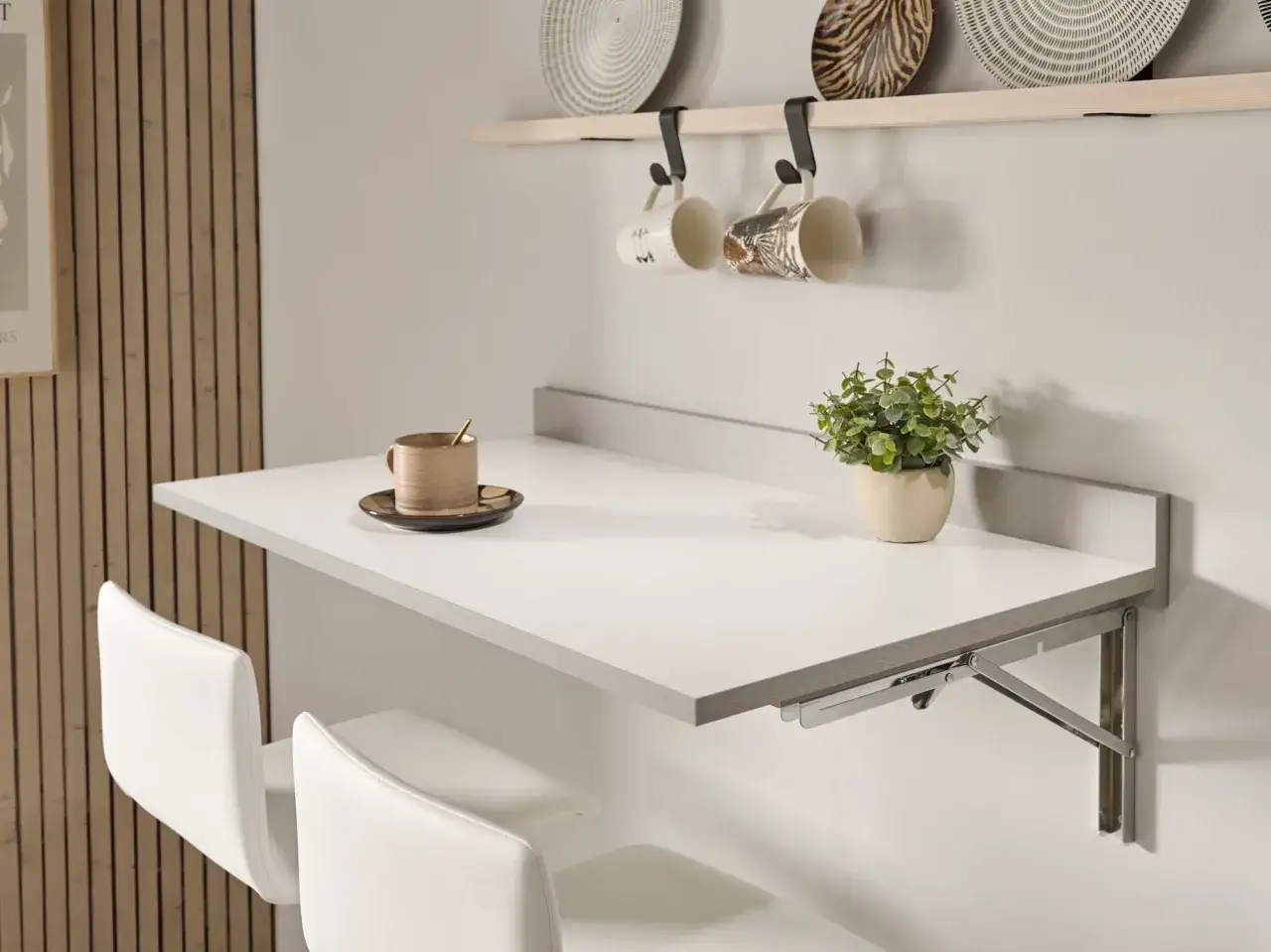 Estilo moderno para mesas para cocinas pequeñas. Una mesa plegable blanca con dos sillas blancas, taza de café y planta.
