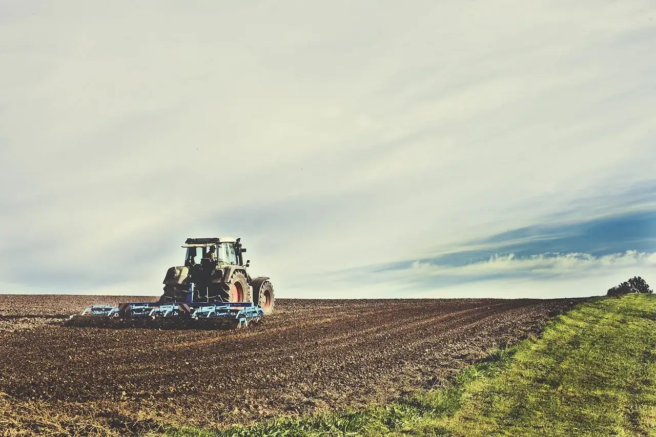 Trattore aratura campo, la suola di lavorazione prepara il terreno per la semina. Cielo nuvoloso.